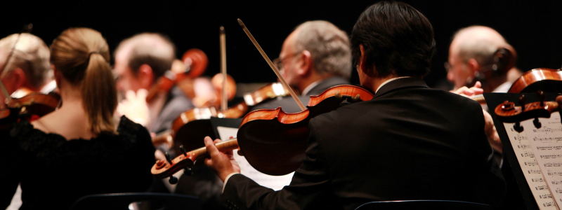 Violinists with the rest of an orchestra performing in the background