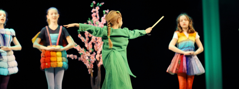 Children in theatre costumes performing a pantomime on stage.